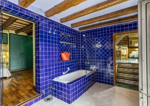 Baño de lujo con azulejos azules, bañera, vigas de madera y ducha de cristal en la casa rural Can Gat Vell, Cataluña