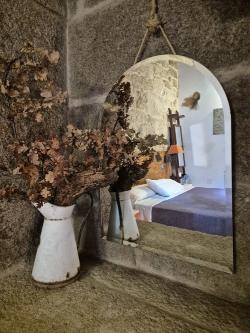 Espejo rústico en Aldea Rural Pazos De Arenteiro con flores secas en jarra blanca y paredes de piedra