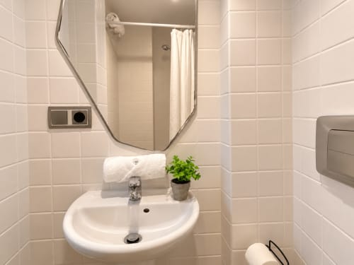 Baño limpio con azulejos blancos, lavamanos, espejo y ducha en estudio Holibai de Baiona
