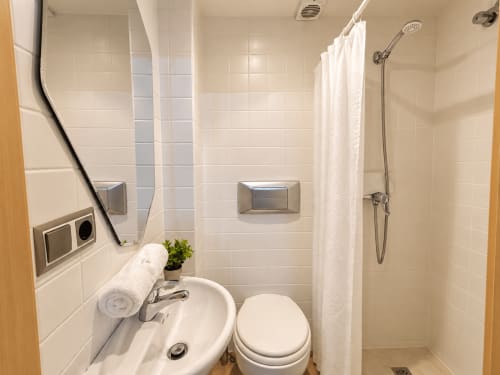 Baño moderno con azulejos blancos, lavabo, inodoro y ducha con cortina en el apartamento Holibai de Baiona