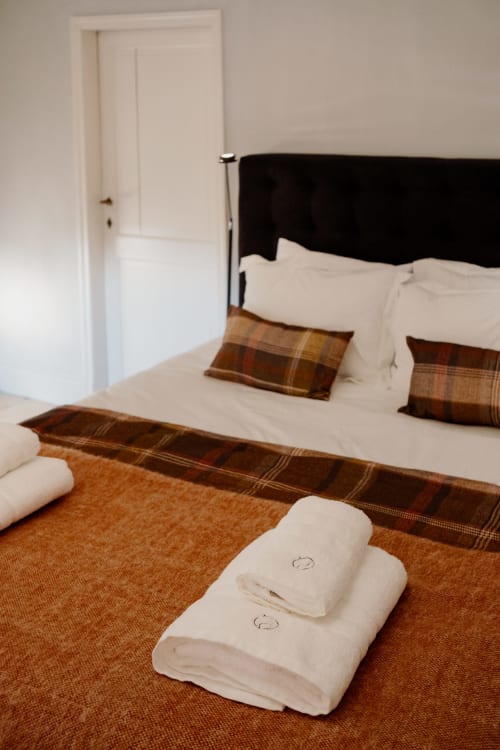 Thérèse Suite bedroom at Castanea Business & Suites with white towels on brown runner, black headboard bed, and cream linens