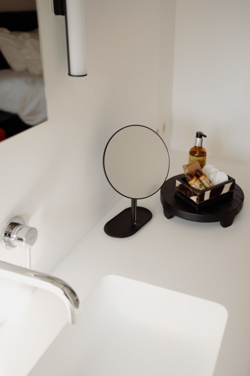 Bathroom vanity at Castanea Business & Suites with round mirror, pump dispenser, and black organizer tray holding toiletries