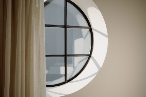 Modern circular window with black grid frame at Castanea Business & Suites in Merelbeke, Belgium, next to cream curtains