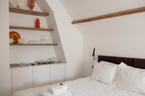 Bright modern bedroom at Castanea Studios with white bedding, wooden beams, built-in shelving, and minimalist decor