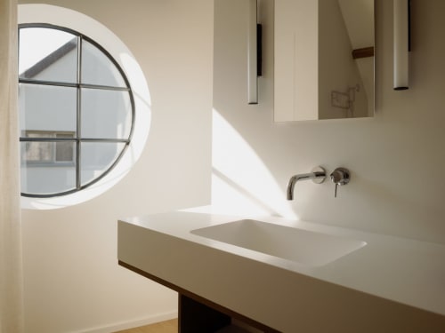 Modern bathroom at Castanea Business & Suites with round window, white sink countertop, and wall-mounted faucet in Studio