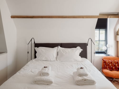 Modern bedroom with white bedding, dark headboard, and exposed wooden beam at Castanea Business & Suites, Merelbeke