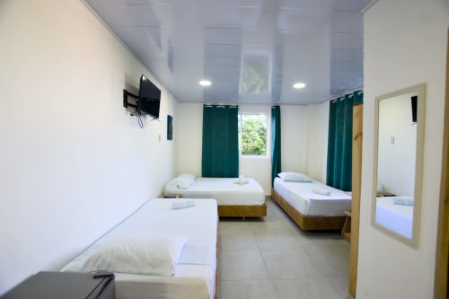 Luminosa habitación con cuatro camas individuales, TV, aire acondicionado y cortinas verdes en Vamos pa San Andrés Isla