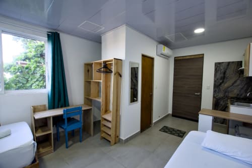 Moderna habitación en Vamos pa San Andrés Isla con camas, escritorio, armario, TV y ventana con vista al mar y cortinas turquesas