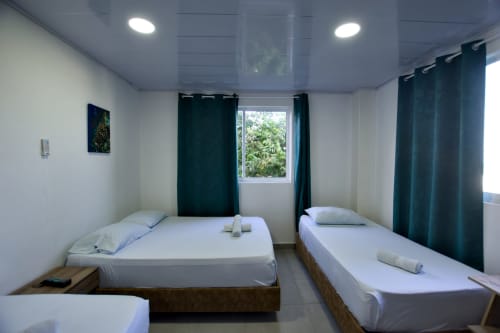 Camas gemelas en habitación luminosa de Vamos pa San Andrés Isla con cortinas verde oscuro y ventana con vista al mar, San Andrés