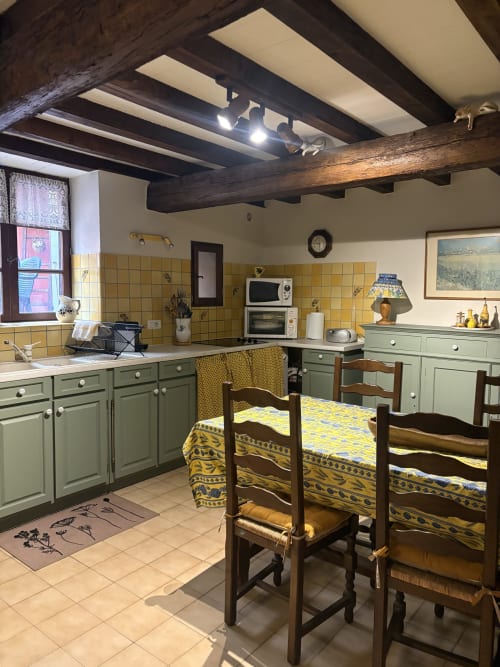 Cuisine rustique d'Arles avec carrelage jaune, meubles verts, poutres apparentes, table à manger et chaises en tissu jaune
