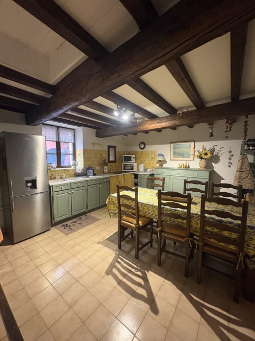 Cuisine rustique d'Arles avec poutres apparentes, carrelage jaune, armoires vertes, table à manger et électroménager inox