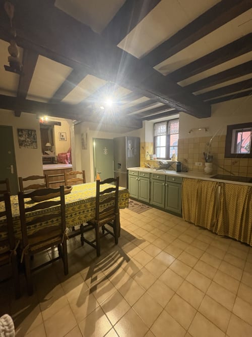 Cuisine-séjour lumineux dans un gîte d'Arles avec poutres apparentes, meubles verts, table à manger et accès à la chambre