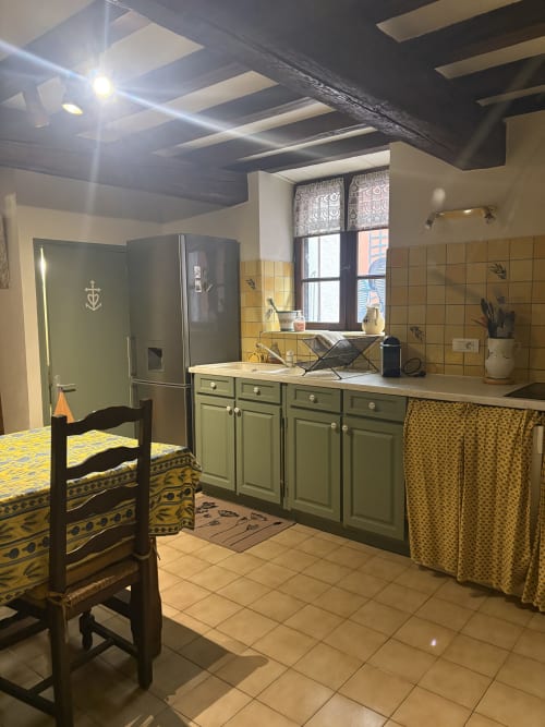 Cuisine provençale d'Arles avec armoires vertes, carrelage jaune, poutres apparentes et coin repas