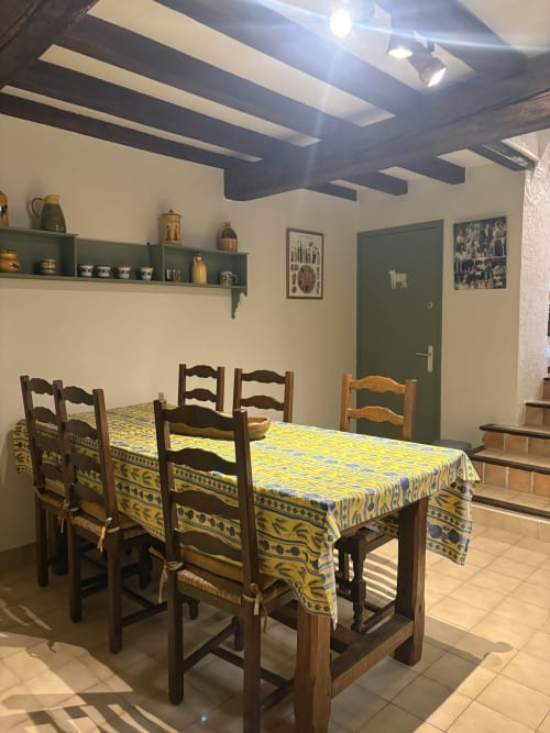 Salle à manger de location vacances à Arles avec nappe jaune à motifs, chaises en bois, poutres apparentes et porte verte