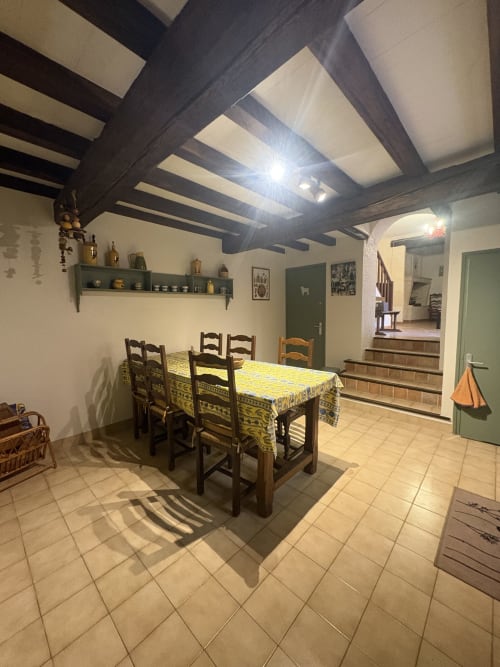 Salle à manger dans une maison d'Arles avec plafond à poutres en bois, table nappage jaune et chaises rustiques