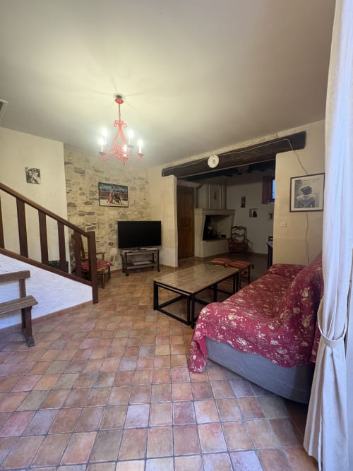 Grand séjour dans une maison d'Arles avec canapé rouge, TV, carrelage en terre cuite, murs en pierre et escalier en bois