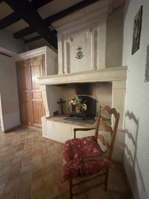 Chapelle rustique d'Arles avec cheminée, poutres en bois, crucifix, fleurs et chaise à dossier échelle avec coussin rouge