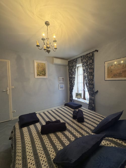Chambre avec lits jumeaux, draps rayés, lustre, rideaux à motifs sombres, œuvres encadrées dans une chambre d'hôtel à Arles