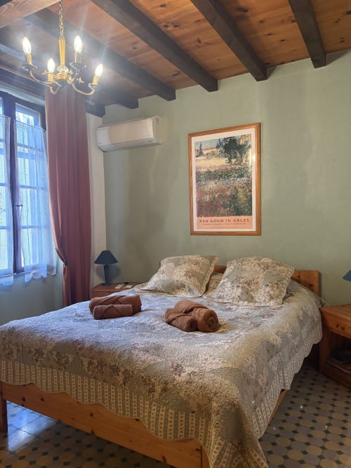 Chambre ensoleillée à Arles avec plafond à poutres apparentes, affiche Van Gogh encadrée et literie crème de style provençal traditionnel.