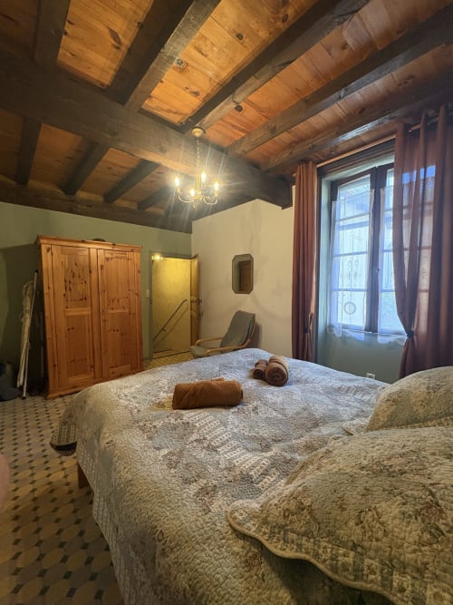 Chambre spacieuse à Arles avec poutres apparentes, lits jumeaux draps crème, armoire bois, portes vitrées ouvertes