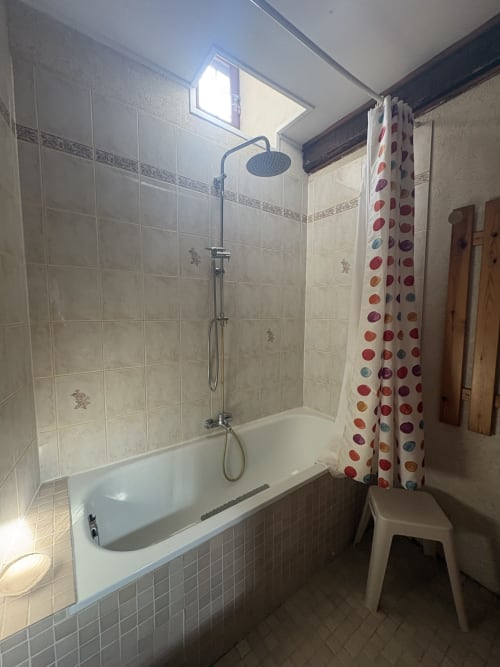 Salle de bains moderne avec baignoire, douche pluie et rideau à pois colorés à la Conciergerie Maurin, Arles