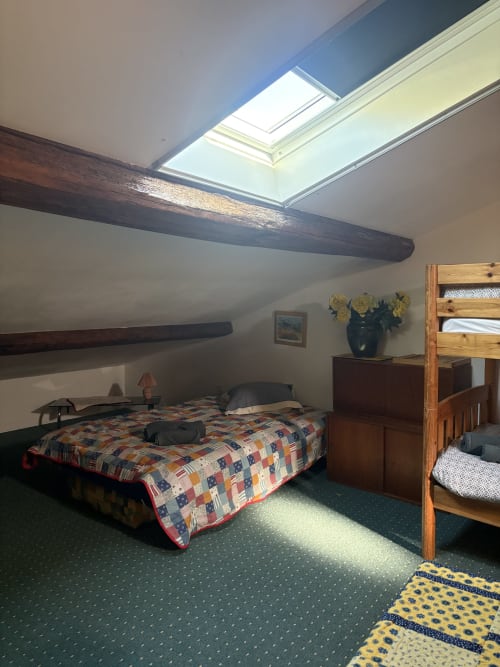 Chambre mansardée à Arles avec puits de lumière, poutres apparentes, lit à courtepointe, meubles en bois et moquette verte