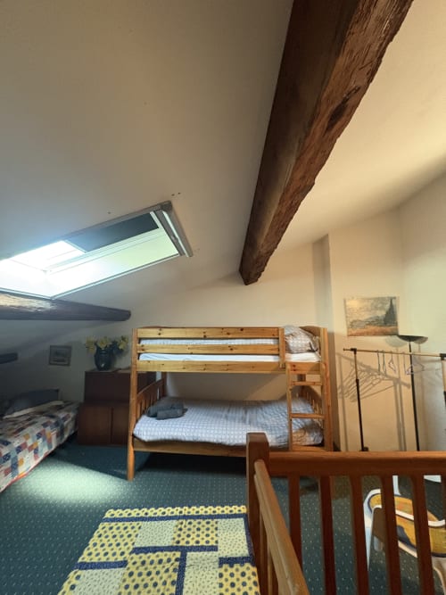 Chambre mansardée lumineuse avec lits superposés en bois, puits de lumière, poutre apparente et tapis jaune à motifs à Arles