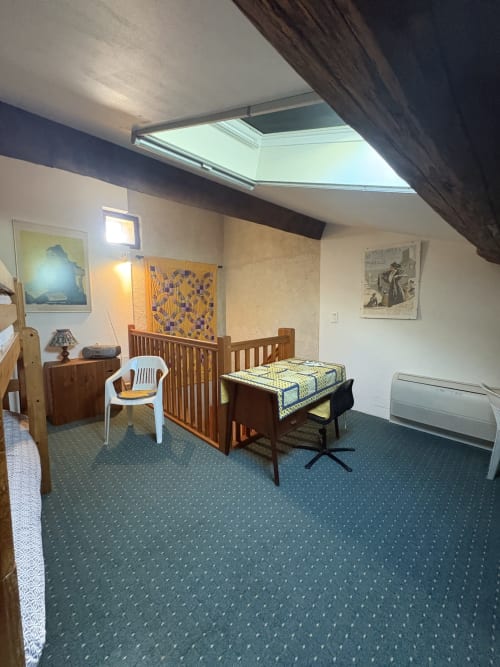 Chambre spacieuse sous les toits avec lucarnes, lit bébé en bois, lit, chaise blanche et moquette bleue dans propriété d'Arles