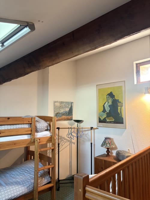 Chambre cosy avec lits superposés en bois, plafond aux poutres apparentes foncées, et œuvres encadrées dans une maison d'hôtes à Arles
