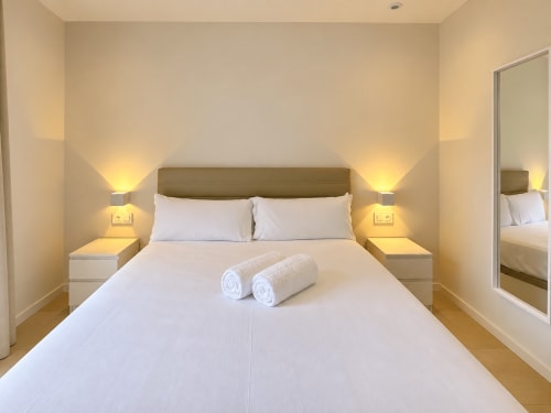 Habitación accesible moderna del hotel Holibai en Baiona con cama queen, sábanas blancas, toallas enrolladas e iluminación ambiental