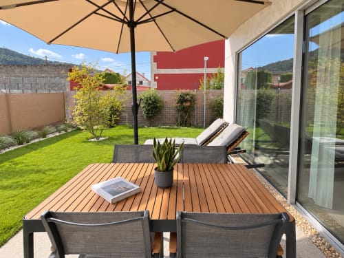 Terraza del apartamento Holibai en Baiona con zona de comedor, tumbonas de jardín, sombrilla y vistas al jardín paisajístico