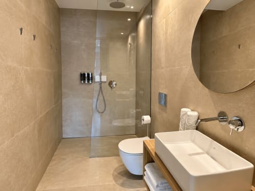 Baño moderno del apartamento Holibai en Baiona, con ducha a ras de suelo, lavabo de cerámica blanco, inodoro y espejo redondo