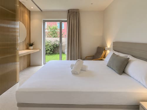 Dormitorio moderno y luminoso con vistas al jardín, cama blanca, cabecero gris, detalles de madera y puertas al patio