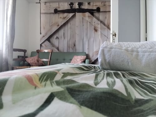 Quarto aconchegante na Maison de Barlest com sofá verde, roupa de cama floral e cabeceira de porta de celeiro rústica.