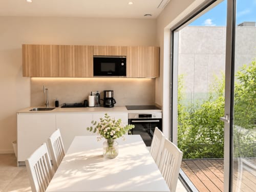 Moderna cocina y zona de comedor en Baiona con muebles de madera, mesa blanca y acceso a terraza en Holibai