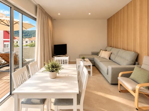 Moderno salón de apartamento en Holibai, Baiona con sofá gris, mesa de comedor, TV y terraza con vistas a la ciudad