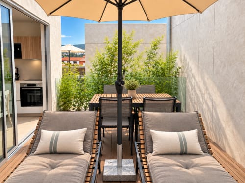 Terraza moderna del apartamento Holibai Baiona con tumbonas, sombrilla, mesa de comedor y vistas a la costa gallega.