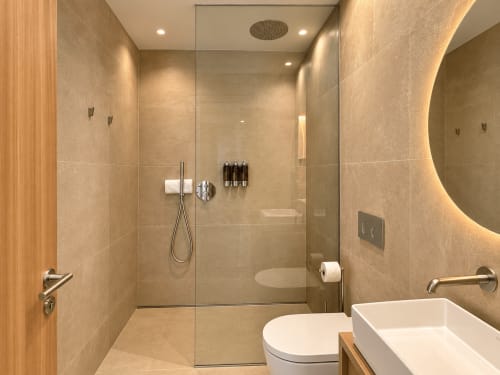 Baño moderno en apartamento Holibai de Baiona con ducha a ras de suelo, lavabo blanco y espejo calefactado
