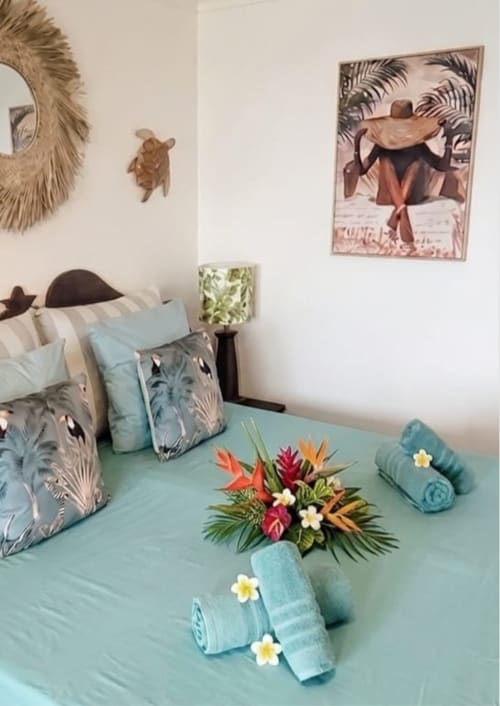 Chambre tropicale à Ti Oasis Sainte-Luce avec literie turquoise, arrangement floral coloré, serviettes roulées et