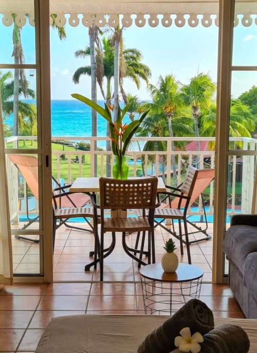 Balcon de l'appartement MADIANA à Ti Oasis avec vue mer, palmiers, piscine et mobilier de détente à Sainte-Luce