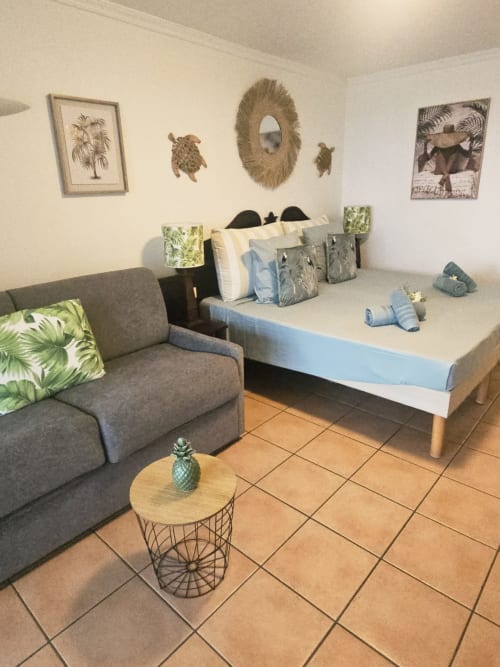 Chambre MADIANA avec canapé gris, lit queen, décoration murale tropicale et carrelage en terre cuite chez TI OASIS