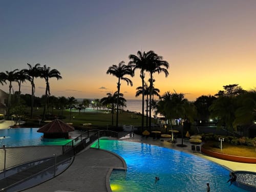 Piscine du resort Ti Oasis au coucher de soleil à Sainte-Luce avec palmiers, vue sur l'océan et eaux illuminées