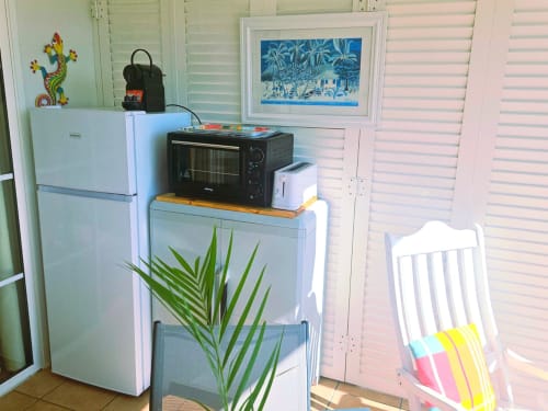 Kitchenette de l'appartement Ti Oasis Trinidad avec micro-ondes, réfrigérateur et décor végétal tropical à Sainte-Luce