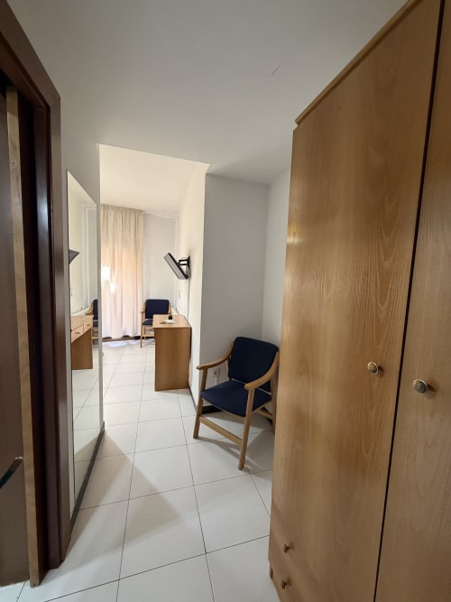 Pasillo del Hotel JM El Emigrante con armario de madera, silla y entrada al dormitorio doble