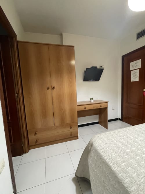 Habitación espaciosa del Hotel JM El Emigrante con armario de madera, escritorio y cama queen en piso de cerámica