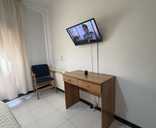Habitación doble del Hotel JM El Emigrante con escritorio de madera, TV mural, silla y radiador en Villanueva de la Serena