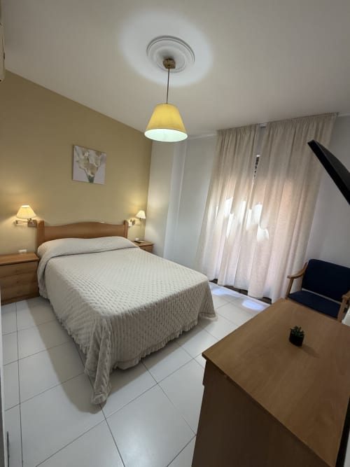 Luminosa habitación doble en Hotel JM El Emigrante con cama queen, lámpara colgante y cortinas translúcidas
