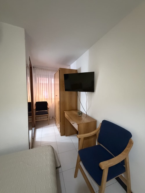 Habitación doble del Hotel JM El Emigrante con TV, muebles de madera, silla azul y vista al pasillo en Villanueva de la Serena