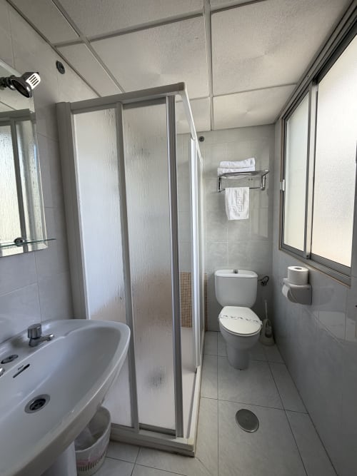 Baño moderno del Hotel JM El Emigrante en Villanueva de la Serena con ducha, inodoro, lavabo y toallas blancas