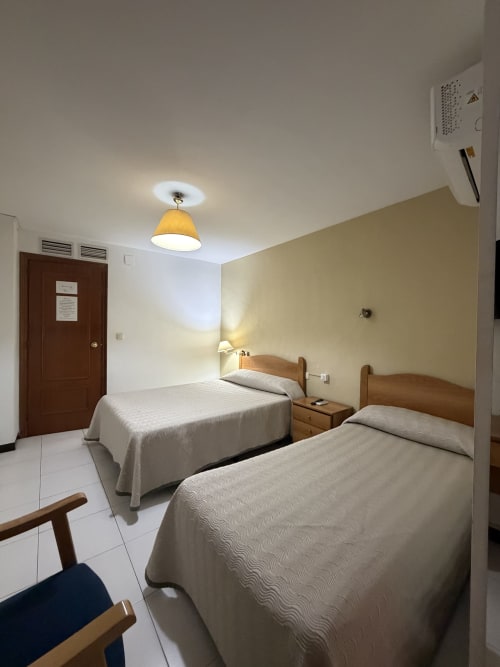 Habitación doble del Hotel JM El Emigrante en Villanueva de la Serena con dos camas, muebles de madera e iluminación moderna